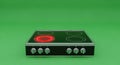 Modern Electric Stove Top with Glowing Red Heating Element and Chrome Knobs on Green Background Royalty Free Stock Photo