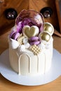 Modern elegant cake with melted white chocolate, golden heart and chocolate balls, macaroons, meringue and caramel.