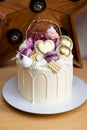 Modern elegant cake with melted white chocolate, golden heart and chocolate balls, macaroons, meringue and caramel.