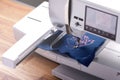 Modern embroidery machine stitching light pink magnolia graphic on classic blue boiled wool on wooden work bench Royalty Free Stock Photo