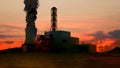 Factory site with smoke from pipe going up against sky. Power plant building with black smoke over evening sky