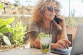 Modern entrepreneur businesswoman working on laptop at the cafe beach bar writing and speaking on phone call. Busy modern woman Royalty Free Stock Photo