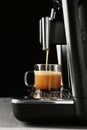 Modern espresso machine pouring coffee into glass cup on grey table against black background Royalty Free Stock Photo