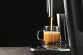 Modern espresso machine pouring coffee into glass cup on grey table against black background. Space for text Royalty Free Stock Photo