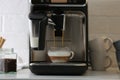 Modern espresso machine pouring coffee into glass cup with milk on white countertop in kitchen Royalty Free Stock Photo