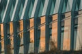 Modern facade of a building made of glass and metal, with reflection of sunset and trees visible in the glass Royalty Free Stock Photo