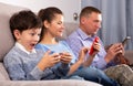 Modern family sitting with smartphones in home interior Royalty Free Stock Photo