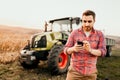 Modern farmer working and harvesting using smartphone in modern agriculture with tractor background