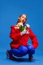 modern fashion. Beauty inside. Weird girl in blue tights with flowers in unusual, strange, red jacket sitting against Royalty Free Stock Photo