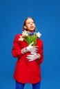 modern fashion. Beauty inside. Weird girl with flowers in unusual, strange, red jacket posing against blue color studio Royalty Free Stock Photo