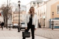 Modern fashion model of a young woman in a white fashionable jacket in stylish jeans with a leather trendy bag stands on the Royalty Free Stock Photo