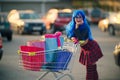Modern, fashionable woman with blue hair, standing in the car park with a shopping trolley full. A concept sale in the
