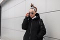 Modern fashionable young woman hipster with stylish hairstyle in black glasses in a stylish long black coat with a bandana Royalty Free Stock Photo