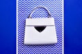 Modern female top-handle bag from white leather with black trim, metal detail, and feet isolated on a blue-white background with a Royalty Free Stock Photo