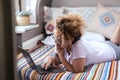 Modern female worker using laptop laying on bed inside camper van bedroom. traveler digital nomad lifestyle. Living off grid.