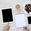 Modern feminine workspace with female hands, smartphone, tablet, notepad, berries and latte over white wooden background. Overhead Royalty Free Stock Photo