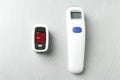 Modern fingertip pulse oximeter and non contact infrared thermometer on grey stone background, flat lay