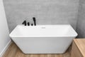 A modern, free standing wall mounted bathtub with a black matt tap, standing in a bathroom lined with ceramic tiles. Royalty Free Stock Photo