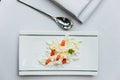 Modern French appetizer: crush and cut cheese with diced tomato served on white rectangle plate with silver spoon and napkin Royalty Free Stock Photo