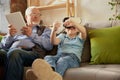 Portrait of happy senior man and little boy, grandfather and grandson using VR glasses sitting on sofa at home and Royalty Free Stock Photo