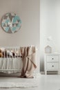 Modern, geometric clock hanging on beige wall in warm baby room interior with white crib. Real photo Royalty Free Stock Photo