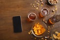 Modern get-togethers in bar. Smartphone, two glasses of beer, bottle, pistachio and chips are scattered on table