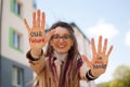 Modern girl with long dreadlocks and eyeglasses in nude color trench is showing hands with written slogan `Our future in Royalty Free Stock Photo