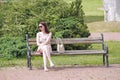 Modern girl sitting on bench in city park. Woman has a rest