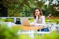 Modern latin curly girl working on laptop while sitting in a street cafe.