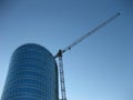 Construction crane next to glass office building on the background of blue skies. Royalty Free Stock Photo