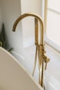 Modern gold faucet from floor and bathtub at big window, modern boho bathroom design. Stylish bathroom interior Royalty Free Stock Photo