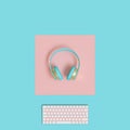 Modern gold and light blue audio headphones and computer keyboard on a two-color background in flat lay style