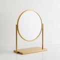 Modern gold tabletop vanity mirror with a circular reflective surface on a white marble surface Royalty Free Stock Photo