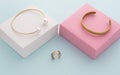 Modern golden bracelets on pink and white boxes and double shape ring on blue background Royalty Free Stock Photo