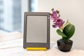 Modern gray electronic book with a blank screen next to an artificial pink orchid on the kitchen table Royalty Free Stock Photo