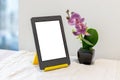 Modern gray electronic book or tablet with a blank mockup screen on a yellow stand next to an artificial pink orchid Royalty Free Stock Photo