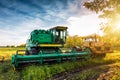 The modern green combine harvester and yellow heavy duty tractor on agricultural field in the rays of the sun Royalty Free Stock Photo