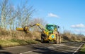 Modern green tractor hedge cutting on road