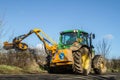 Modern green tractor hedge cutting on road