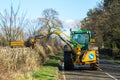 Modern green tractor hedge cutting on road