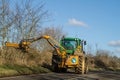 Modern green tractor hedge cutting on road