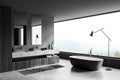 Modern grey bathroom interior with bathtub and washbasin, panoramic window