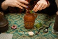 Modern gypsy witch makes love potion. Psychic holds brown pot of drink in which adds magical herbs and mixes it with a wooden