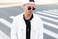 Modern handsome young hipster man in trendy round glasses in a summer white jacket in a trendy baseball cap in a black t-shirt Royalty Free Stock Photo