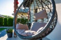 Modern hanging rattan chair with gray pillow and flowers on the summer garden terrace Royalty Free Stock Photo