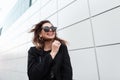 Modern happy young hipster woman in a black stylish coat in dark trendy sunglasses goes and smiles around the city Royalty Free Stock Photo