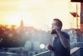Modern happy young man with a beard fun Vaporizers, smoke and bubbles on the terrace. In background, the evening sunset over t