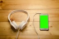 White headphones connected to phone on wooden table. Modern headphone with cable and gadget with green screen Royalty Free Stock Photo