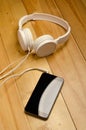 White headphones connected to phone on wooden table. Modern headphone with cable and gadget