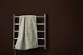 Modern heated towel rail with warm soft towel on brown wall. Space for text